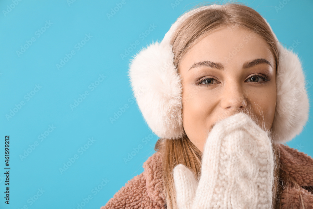 Beautiful woman in mittens and fur earmuffs on blue background Beautiful woman in mittens and fur earmuffs on blue background