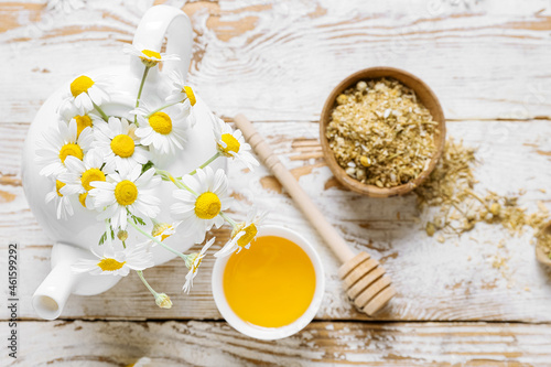 Teapot of fresh chamomile tea with honey and flowers on light wooden background