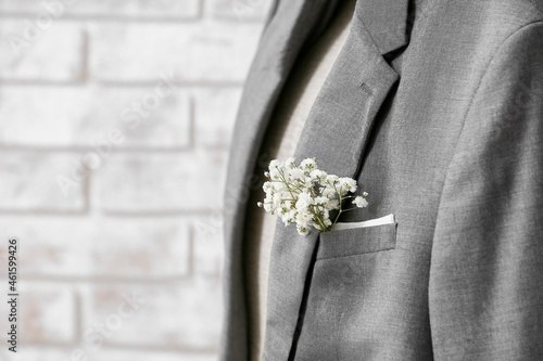 Beautiful gypsophila boutonniere on groom's suit near brick wall, closeup