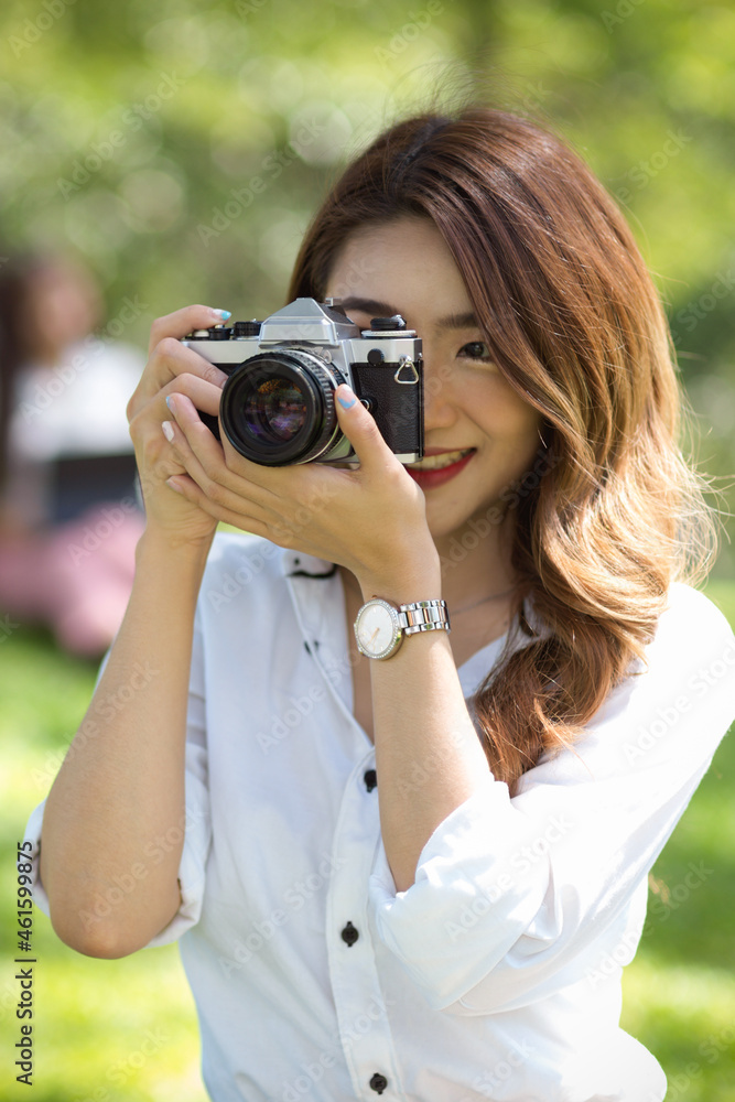 Attractive young female tourist taking a picture by vintage or retro camera in a greenery park