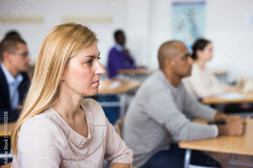Portrait of focused blonde listening to lecture in classroom with group of adult people. Postgraduate education concept