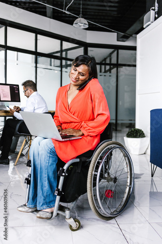 Schilderij op canvas Latin transgender woman sitting in wheelchair using computer while talking on th