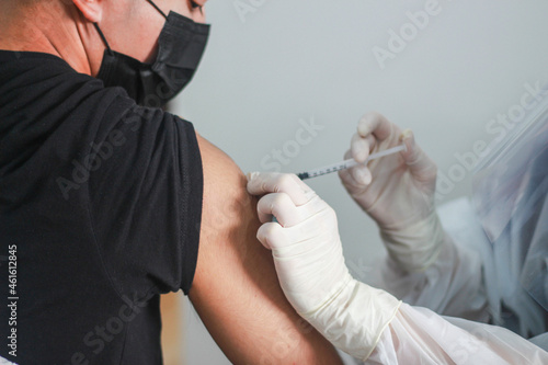 Close up view of an getting vaccine shot in his arm during corona virus pandemic. patient in medical mask. Covid-19 or coronavirus vaccine
