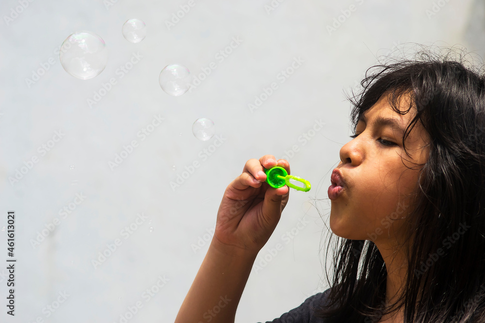 A girl holding a bubble maker and blowing them out. Image focused on the girl. A girl holding a bubble maker and blowing them out. Image focused on the girl.