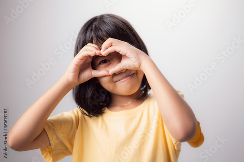 Healthy eyesight and eyes. Portrait of a smiling Asian kid with heart-shaped hands on his eyes. Smiling girl with glowing skin displaying a love symbol. Eye care is very important. photo