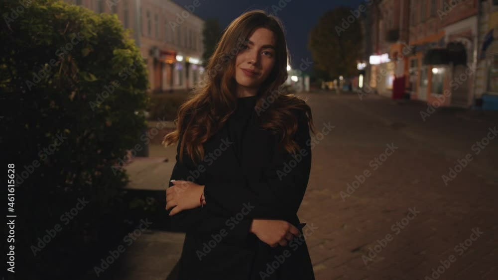 A glamorous young girl stands with her arms crossed on her chest on a city pedestrian street in the late evening. Slow motion A glamorous young girl stands with her arms crossed on her chest on a city pedestrian street in the late evening. Slow motion