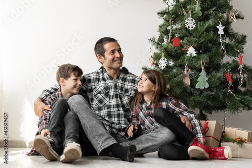 Close-up of a happy family under a tree for Christmas or New Year. Dad with his son and daughter on the floor x-mas in the morning.