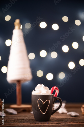 Small cup of hot chocolate with heaping whipped cream decorated with sugar candy cane