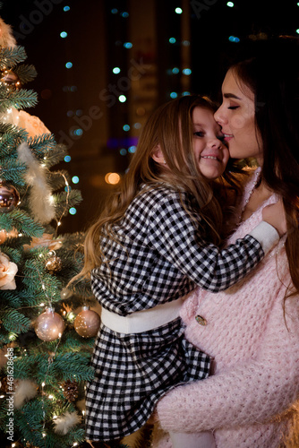 Mom and little daughter in front of the New Year tree at home.