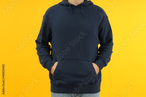 Man in hoodie with hands in pocket on yellow background