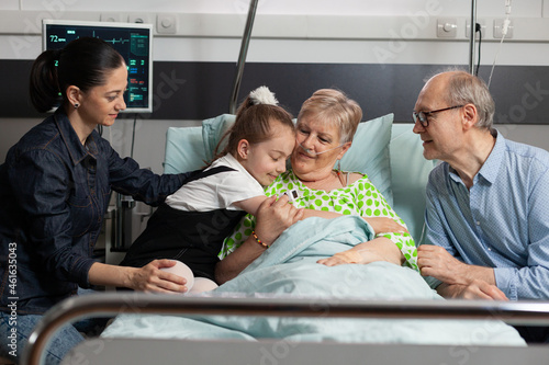 Granddaughter hugging sick elderly grandmother visiting her in hospital ward supporting during clinical recovery. Pensioner senior woman patient resting in bed waiting for healthcare treatment © DC Studio