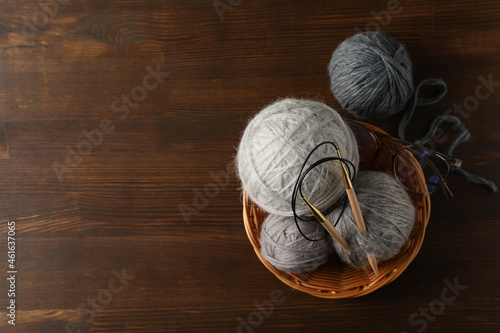 Multi colored balls of yarn with knitting needles in a wicker basket on a wooden background photo