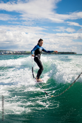 Watersport concept. Young woman in wetsuit learning to wakesurf on the river. Athletic female riding the waves on sunny day.