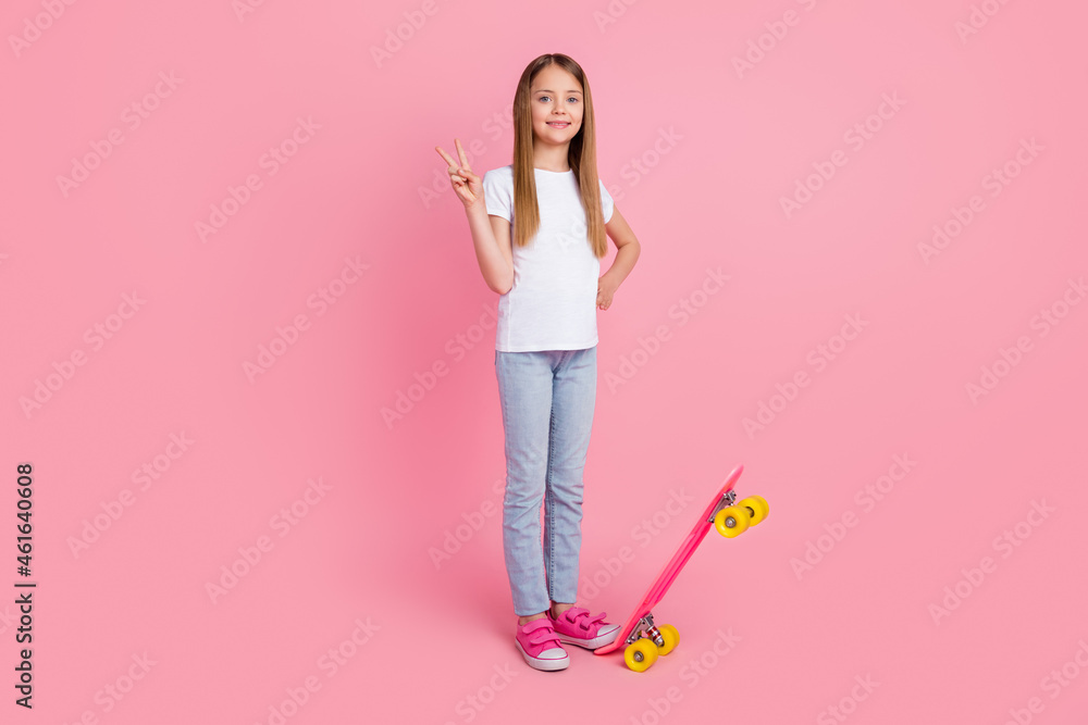Full size photo of funky blond small girl with skate show v-sign wear white t-shirt jeans isolated on pink color background Full size photo of funky blond small girl with skate show v-sign wear white t-shirt jeans isolated on pink color background