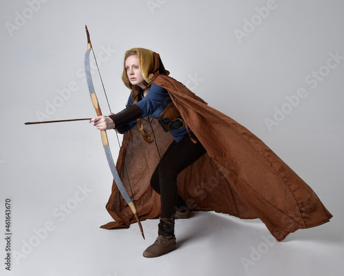 Fotografía Full length, portrait of red haired woman wearing medieval viking inspired costume and flowing cloak,  Holding bow an arrow weapon,  posing against studio background