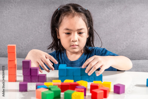 Asian girl plays with small wooden colorful toy blocks at home or kindergarten. A Girl enjoys playing with construction blocks for toddler kids. Education Development Construction creative toys Idea