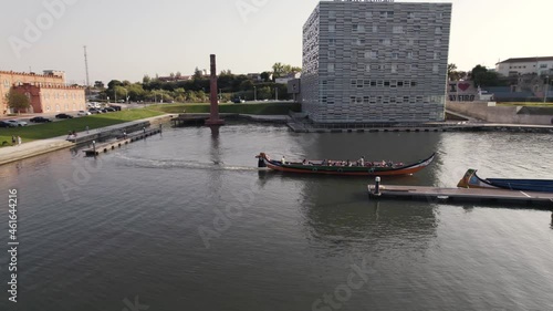 Low level aerial shot following the moving moliceiro boat toward the narrow water canal at Aveiro city.
