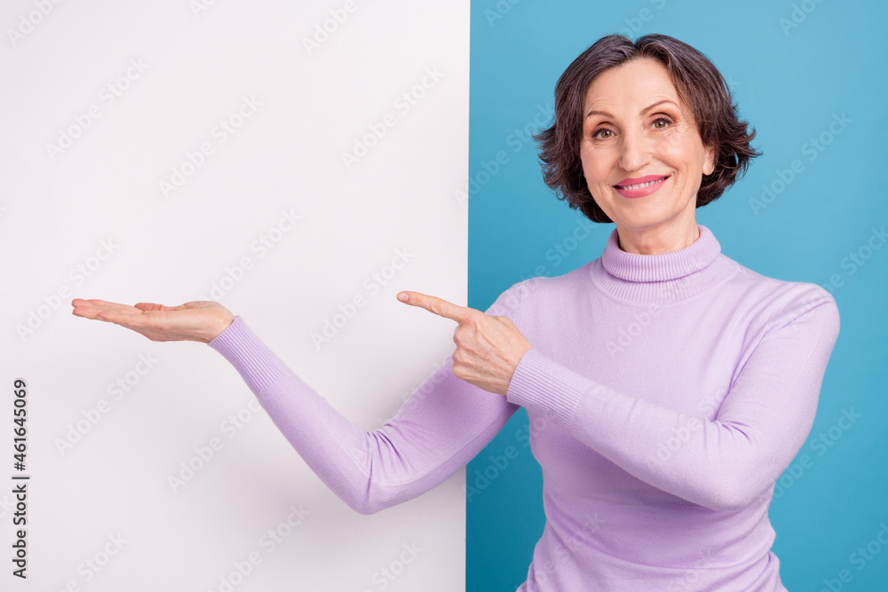 Photo of aged woman happy positive smile point finger product offer advert advice select empty space isolated over blue color background Photo of aged woman happy positive smile point finger product offer advert advice select empty space isolated over blue color background