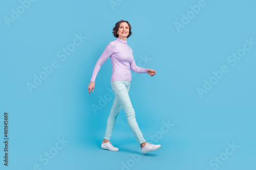 Full length profile side photo of attractive aged woman happy positive smile go walk step isolated over blue color background