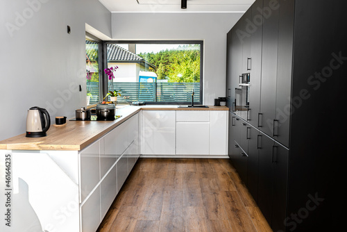 A modern kitchen with white and black fronts and a large corner window  vinyl panels on the floor.