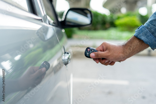 Closes up hand of male key remote unlock the car door before driving. Vehicle transportation travel of gray car on the street road. Travel concept