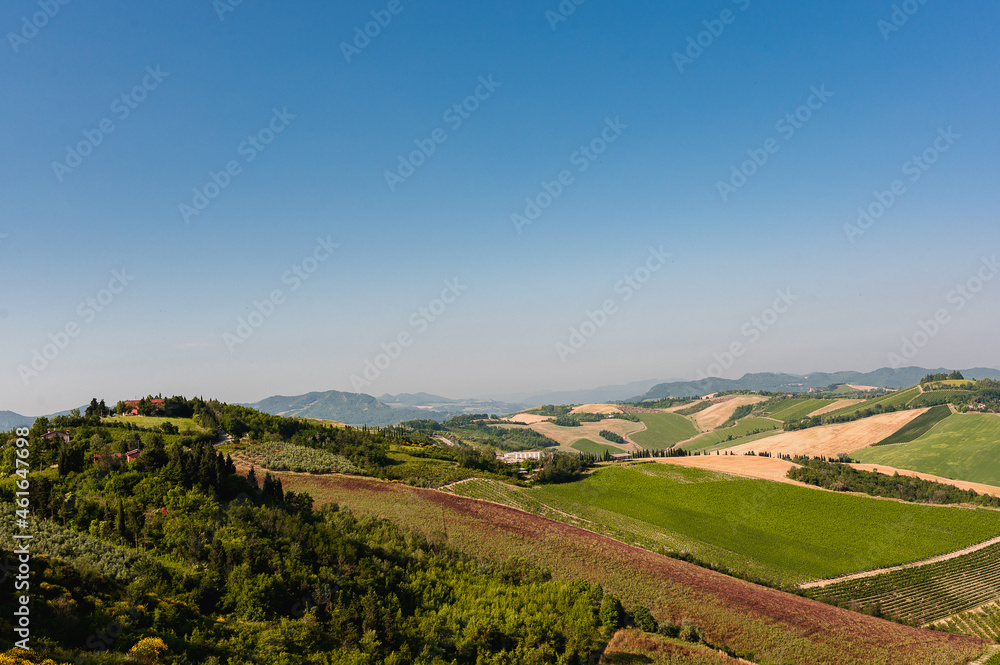 Aerial view of typical Italian landscape with cultivated fields, houses and blue sky.