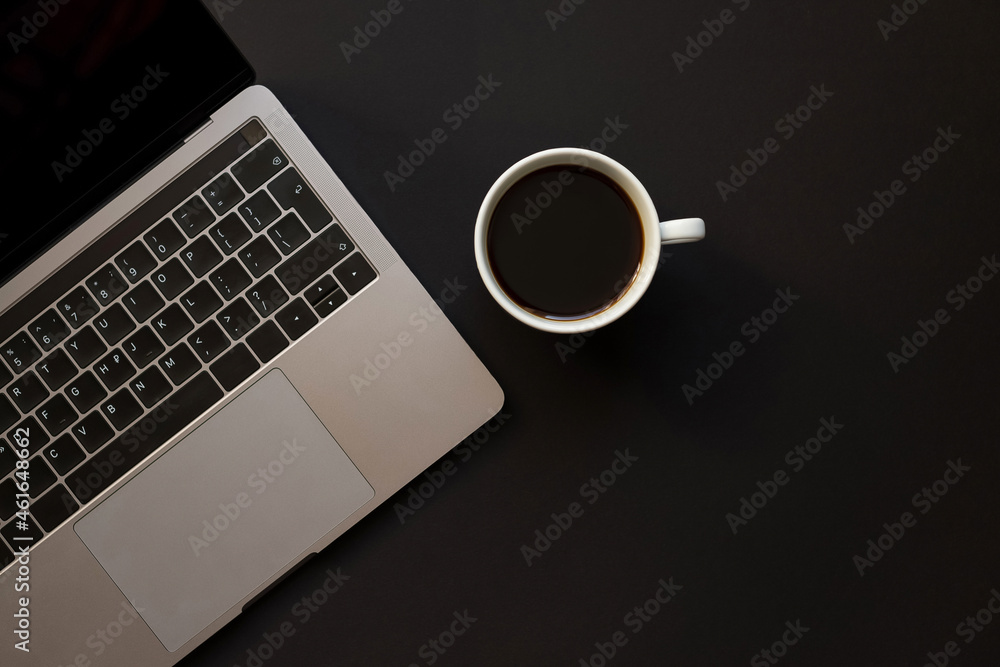 A black desk with a laptop and a cup of coffee. Online work, freelance concept A black desk with a laptop and a cup of coffee. Online work, freelance concept