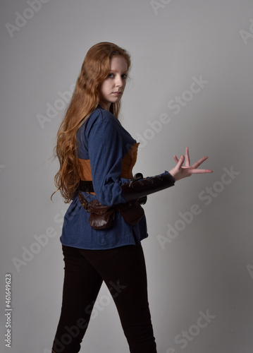 Fotografía Full length portrait of red haired woman wearing medieval viking inspired costume,  Holding a long sword weapon, sitting pose against studio background