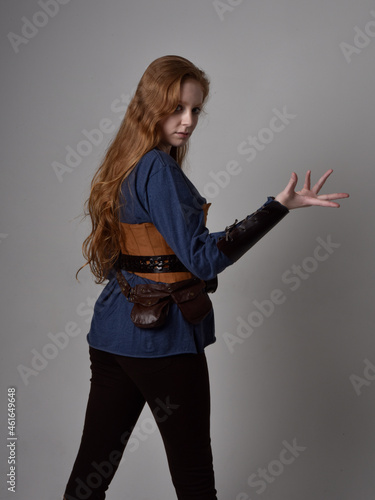 Full length portrait of red haired woman wearing medieval viking inspired costume, Holding a long sword weapon, sitting pose against studio background.