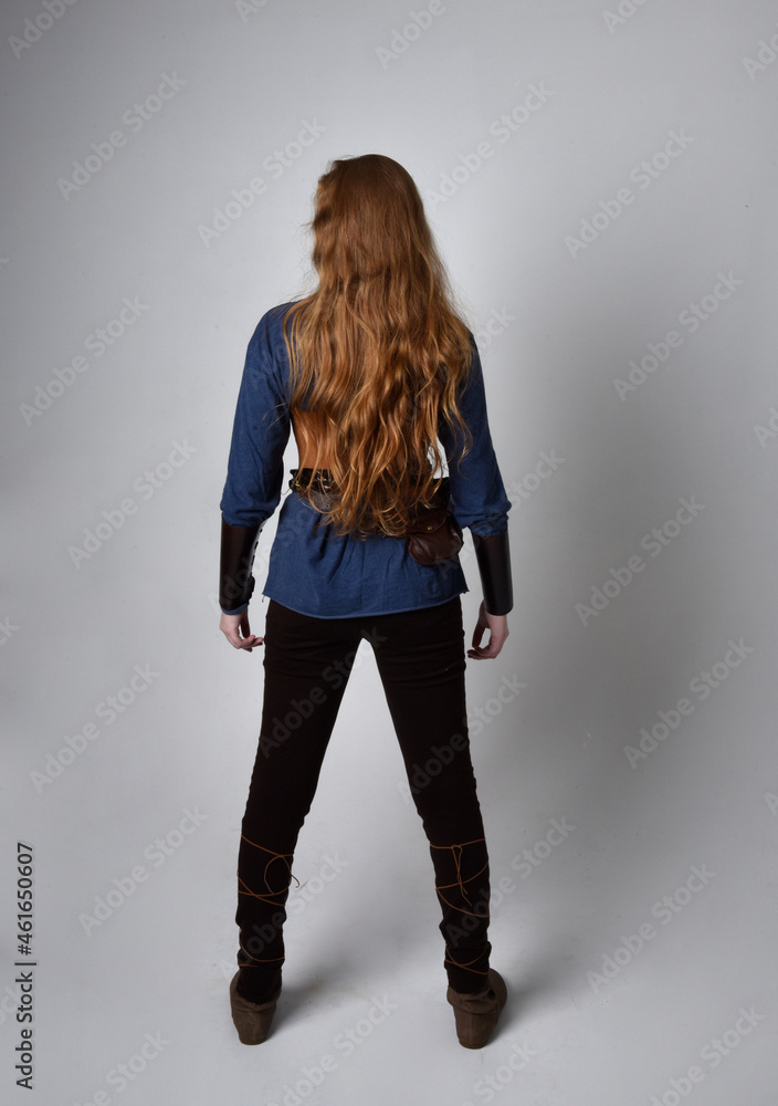 Full length portrait of red haired woman wearing medieval viking inspired costume, standing pose with back to the camera, against studio background. Full length portrait of red haired woman wearing medieval viking inspired costume, standing pose with back to the camera, against studio background.