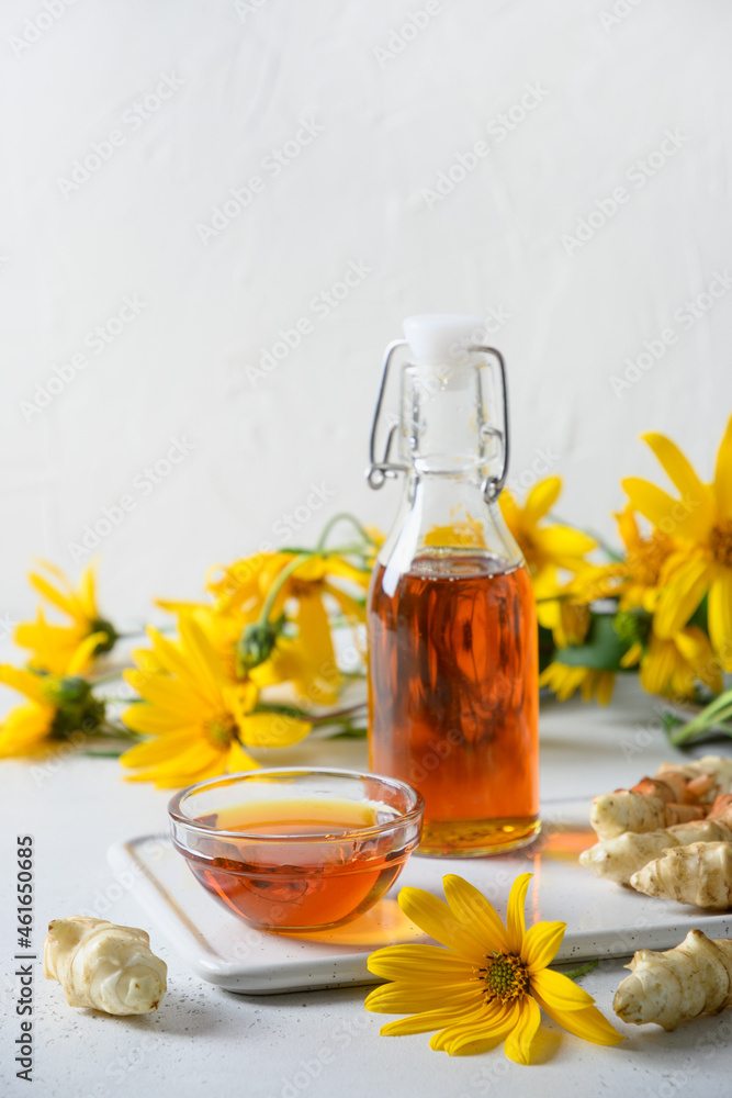 Jerusalem artichoke topinambour syrup in bowl and bottle on white background. Vertical format. Sugar substitute for raw vegan desserts. Jerusalem artichoke topinambour syrup in bowl and bottle on white background. Vertical format. Sugar substitute for raw vegan desserts.