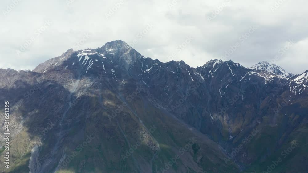 Aerial panoramic view of massive mountain range with traces of snow. Cloudy, overcast sky with shadows on slopes. Slight pan to left. 4k footage. Aerial panoramic view of massive mountain range with traces of snow. Cloudy, overcast sky with shadows on slopes. Slight pan to left. 4k footage.