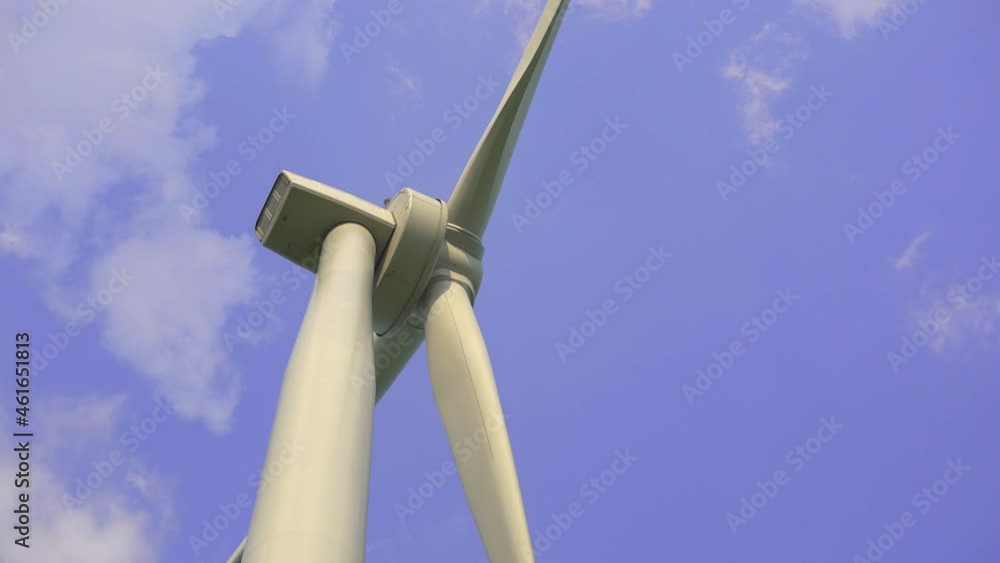 Handheld shot. A wind power turbine with a blue cloudy sky in the background. Investments in green energy. Green electricity concept Handheld shot. A wind power turbine with a blue cloudy sky in the background. Investments in green energy. Green electricity concept