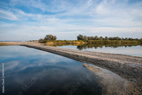 Summer road through the estuary to the sea. Reflection of the blue sky in the water.