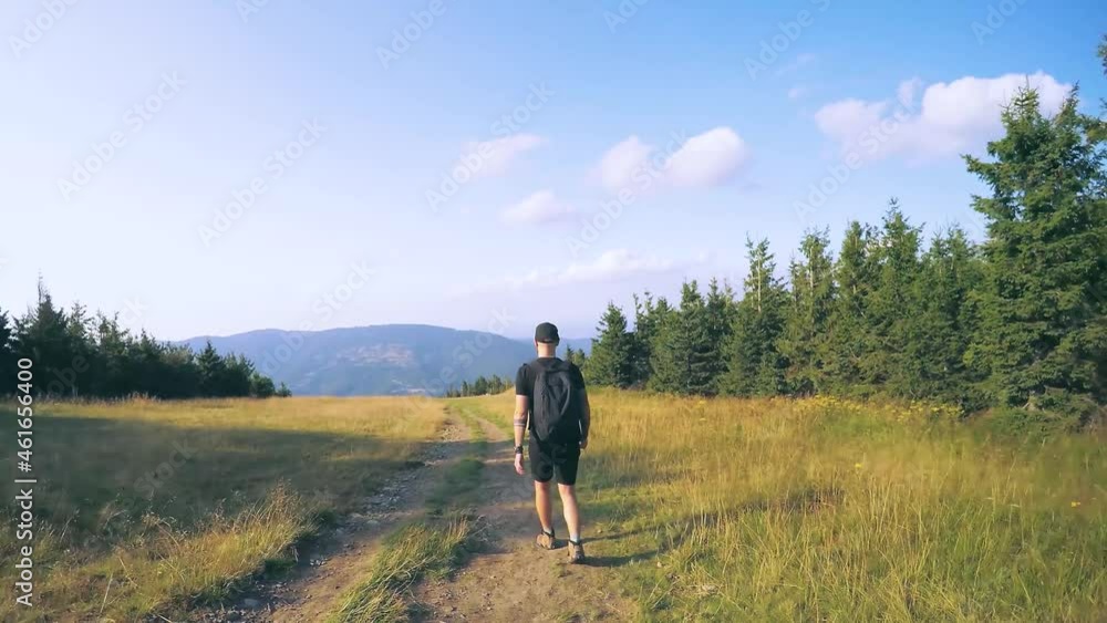 Back View of Walking Person on Mountain Road. Outdoor Activities Travel Concept Man in Nature. 60s Tourist Walks on an Adventure Trip in Natural Landscape in Hike on a Environment. Back View of Walking Person on Mountain Road. Outdoor Activities Travel Concept Man in Nature. 60s Tourist Walks on an Adventure Trip in Natural Landscape in Hike on a Environment.