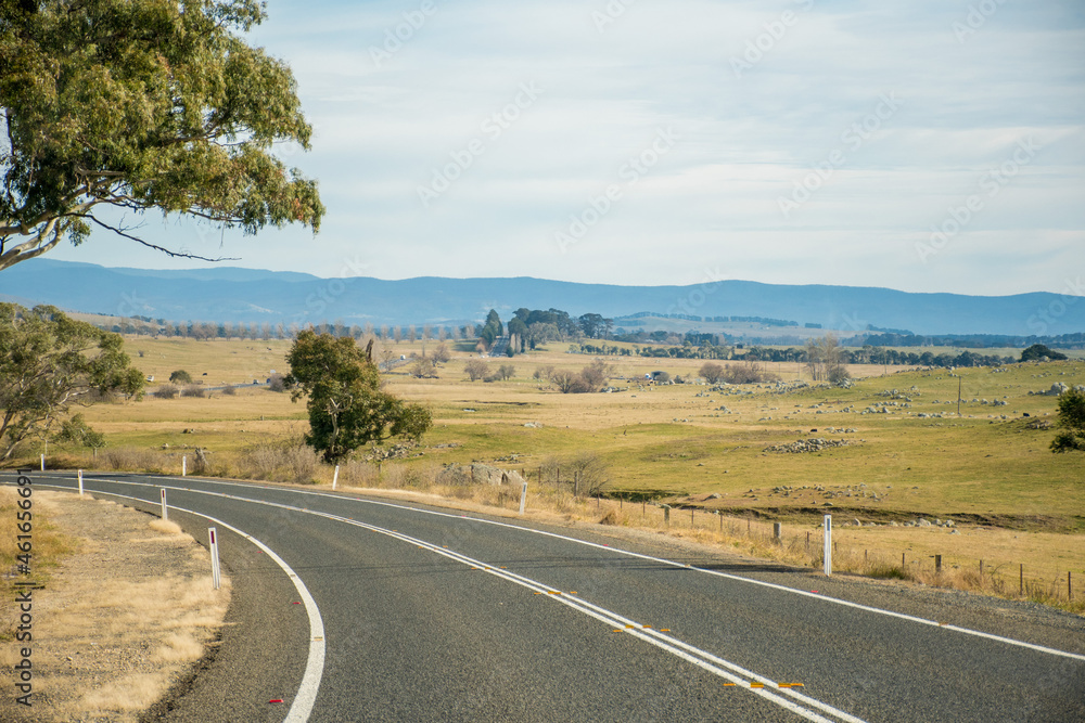 Open empty road surrounded by farms and fields in Australia. Mountains on the horizon. Road trip travel Open empty road surrounded by farms and fields in Australia. Mountains on the horizon. Road trip travel