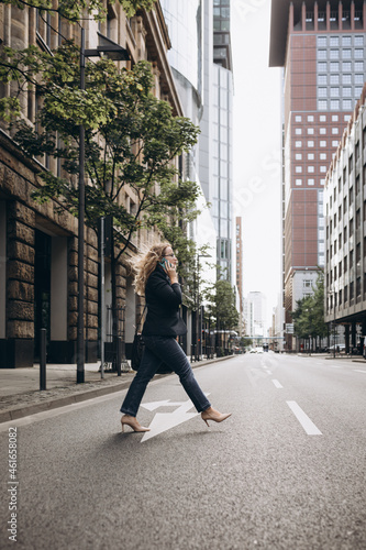 Business woman with big bag and smartphone in hand crosses the street in big city. High quality photo