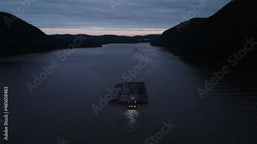 A barge pushing large shipping containers up the Hudson River in New York's hudson valley just after sunset