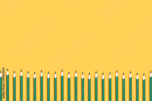 Row of green pencils on a yellow background. Back to school concept.
