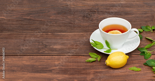 cup of tea with lemon and mint in white cup on wooden brown background