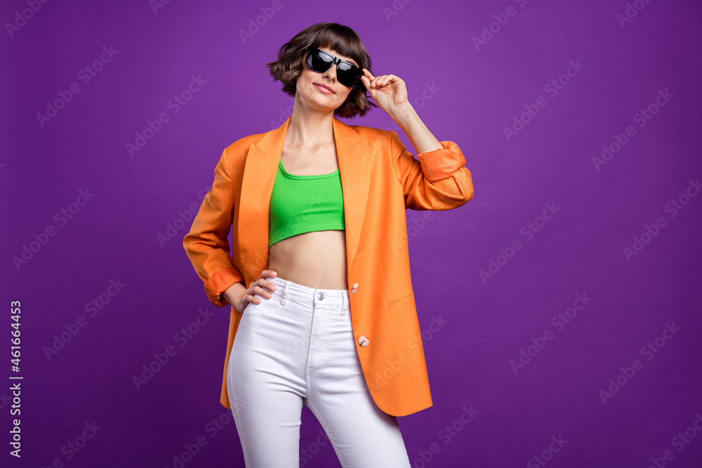 Photo of adorable shiny young woman dressed orange blazer arm dark glasses empty space smiling isolated purple color background Photo of adorable shiny young woman dressed orange blazer arm dark glasses empty space smiling isolated purple color background