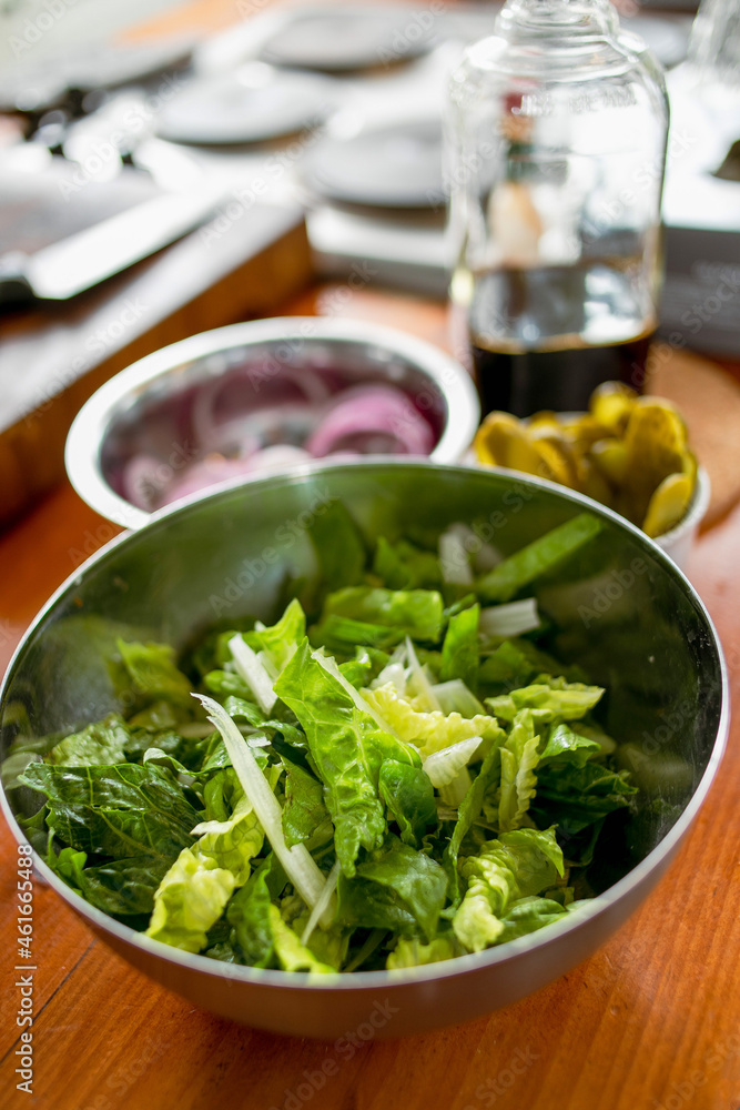 Demonstration of ingredients for cooking in the kitchen on the table. Washed roman salad in a bowl, mixed with celery. Other ingredients and jars in the background. Demonstration of ingredients for cooking in the kitchen on the table. Washed roman salad in a bowl, mixed with celery. Other ingredients and jars in the background.