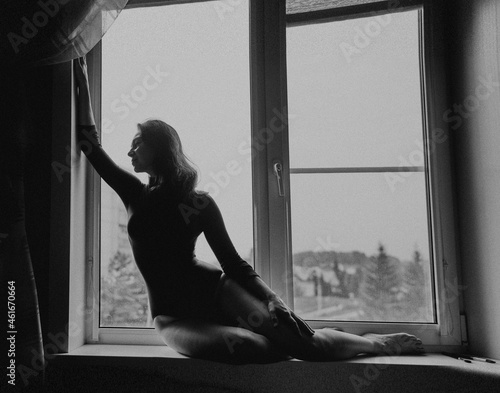 A beautiful girl in a bodysuit sits on the window, black and white photo.