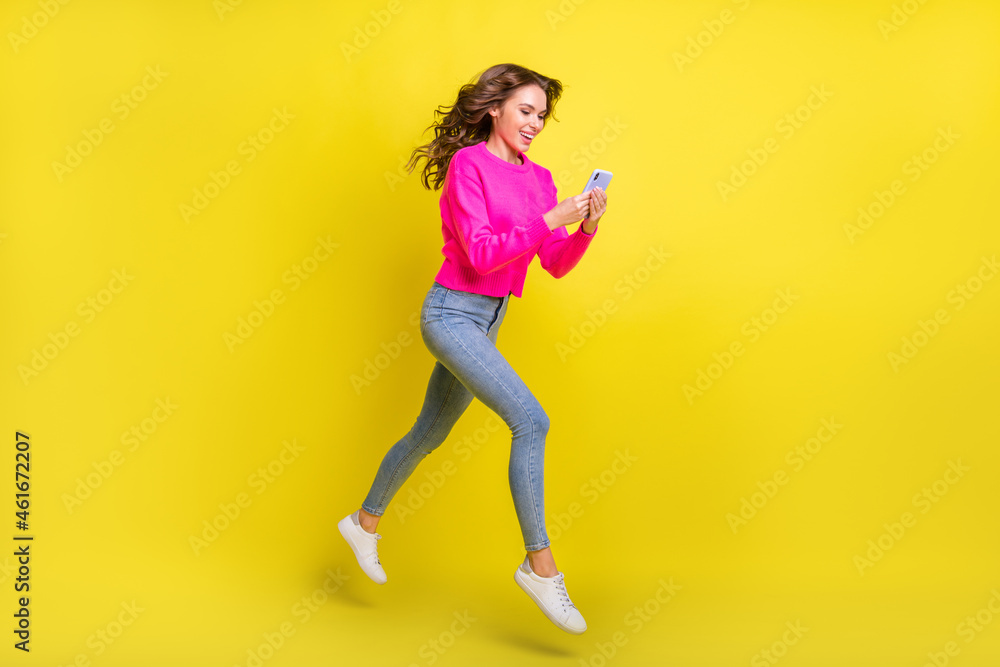 Full size profile size photo of young girl happy positive smile walk jump chat smartphone isolated over yellow color background Full size profile size photo of young girl happy positive smile walk jump chat smartphone isolated over yellow color background