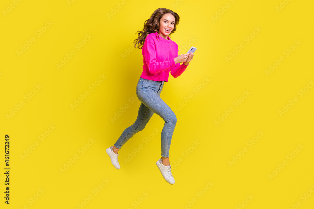 Full length photo of shiny lady dressed pink pullover walking jumping high typing modern device isolated yellow color background