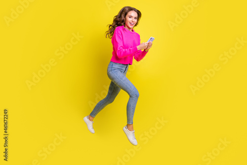 Full length photo of shiny lady dressed pink pullover walking jumping high typing modern device isolated yellow color background