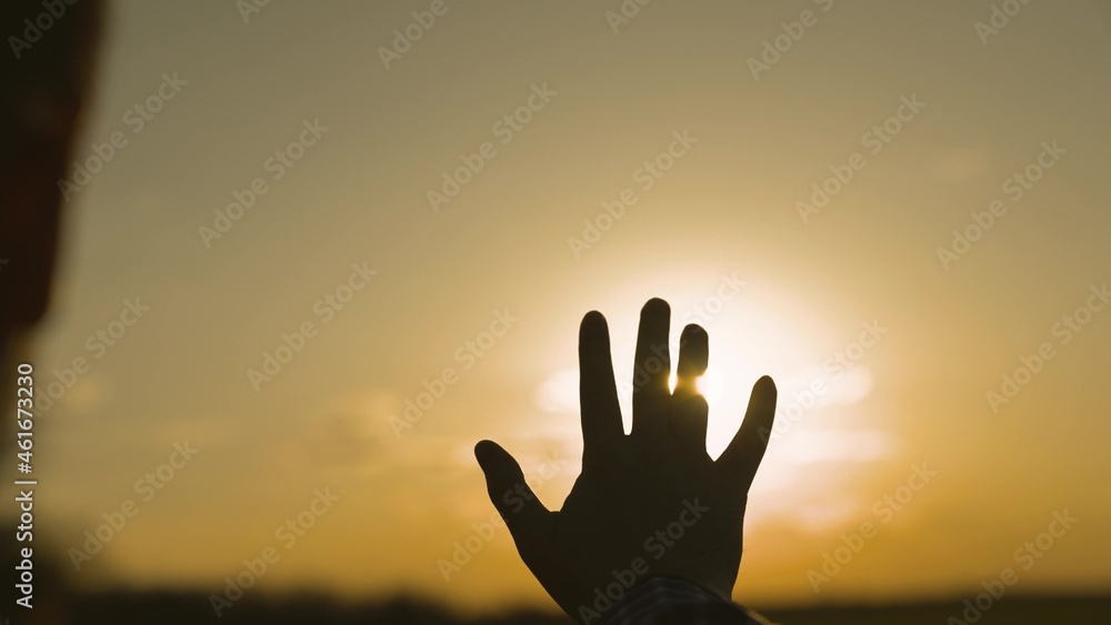 human hand at sunset in the sky, dream of happiness, meditate in the rays of sunlight, catch bright orange light, travel on vacation, harmony of enjoying nature and relaxation, meeting the sunrise
