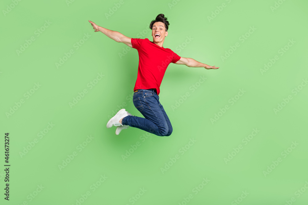 Full size profile side photo of young guy happy smile air flu jump hands wings isolated over green color background Full size profile side photo of young guy happy smile air flu jump hands wings isolated over green color background
