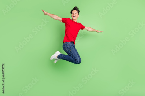 Full size profile side photo of young guy happy smile air flu jump hands wings isolated over green color background