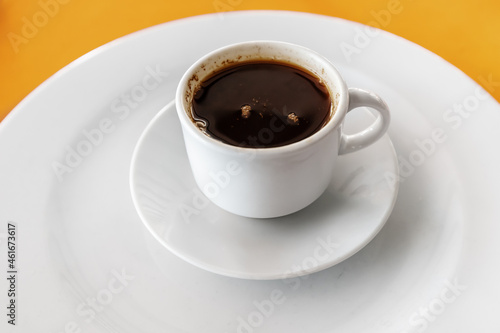 Black hot and fragrant coffee in a mug on a saucer on a bright orange table in the cafeteria